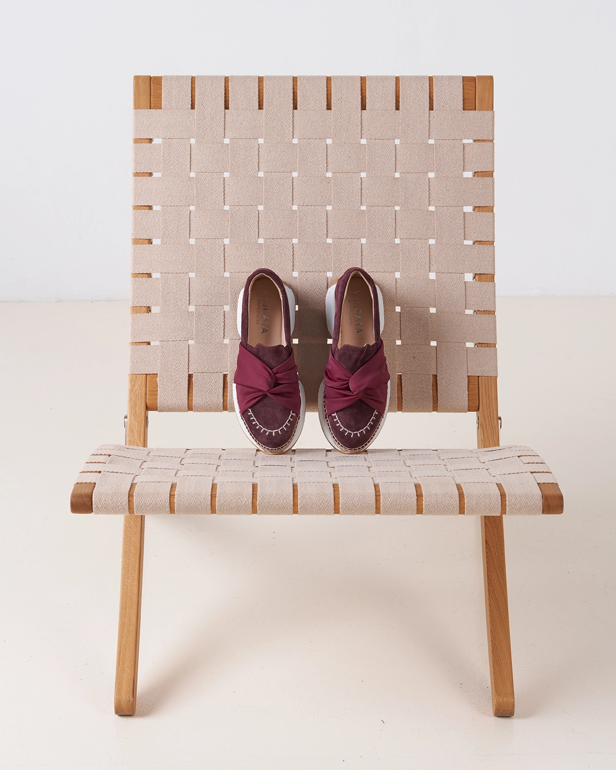 Fotografía de bodegón de zapatos deportivas estilo alpargata color granate sobre silla de diseño, realizada por estudio de fotografía y retoque en Barcelona.