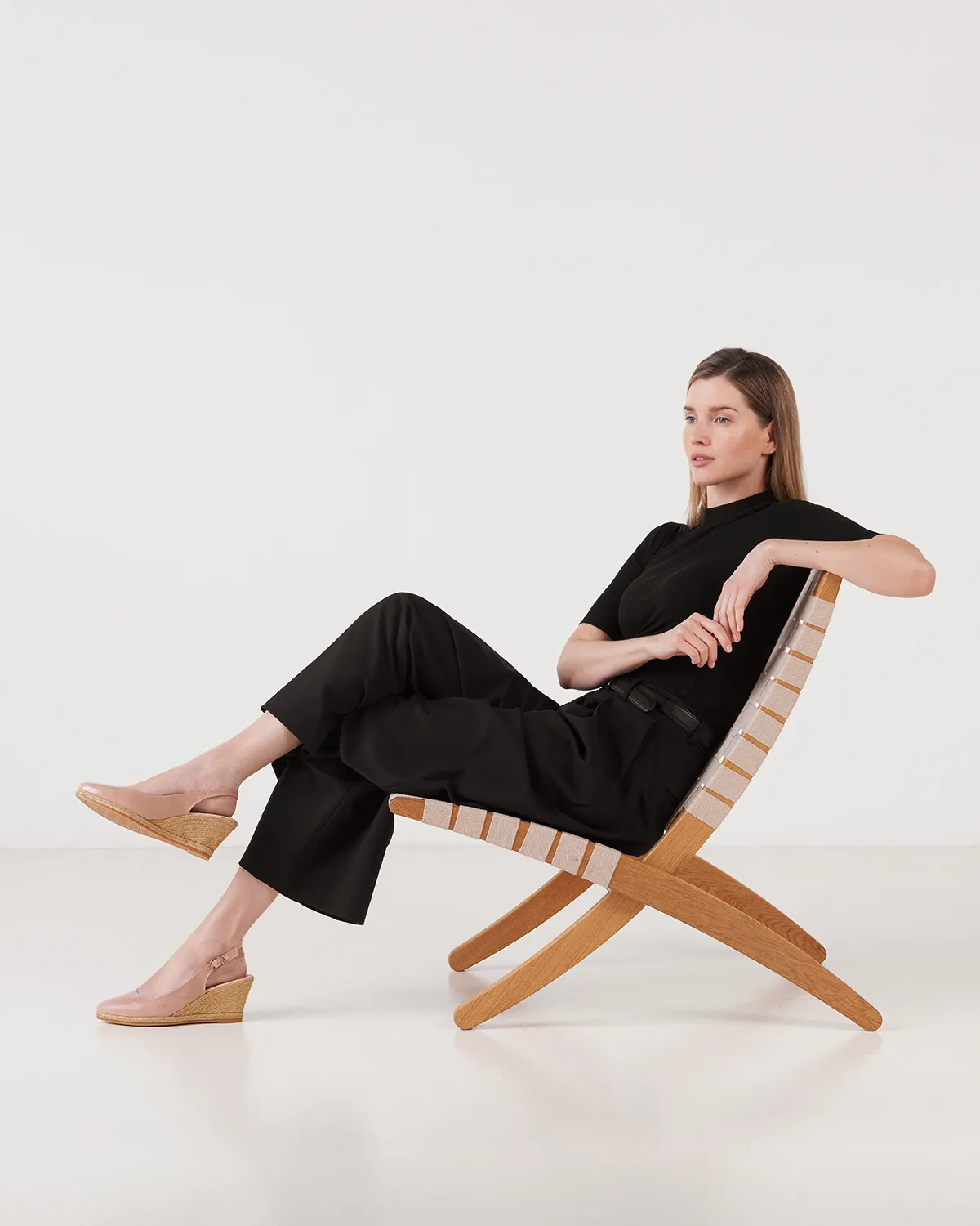 Modelo posando con look total black y alpargatas de cuña en silla de diseño. Fotografía de moda y editorial realizada por Somos Estrategia Visual, estudio de fotografía y retoque en Barcelona.